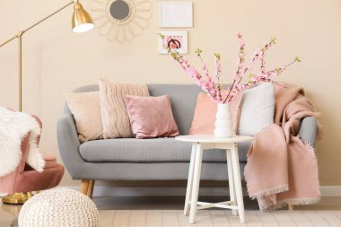 Oturma odasının içinde, kanepede ve vazoda pembe çiçekli dallarla.