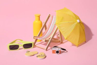 Yaz kompozisyonu, pembe arka planda güneş kremi ve plaj aksesuarları.