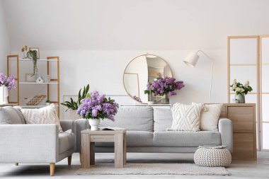 Oturma odasının içinde, vazolarda leylak çiçekleri var.