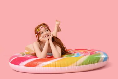 Küçük kızıl saçlı kız pembe arka planda şişme yatakta yatıyor.