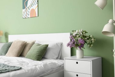 Yatağın yanındaki yeşil duvarın yanında güzel çiçekli vazo, yakın plan.