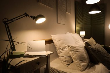 Gece yatak odasındaki masada kitap olan parlak lamba.