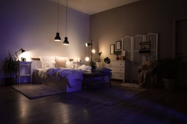 Katlanan perdeli, koltuklu ve parlayan lambalı karanlık yatak odasının içi.