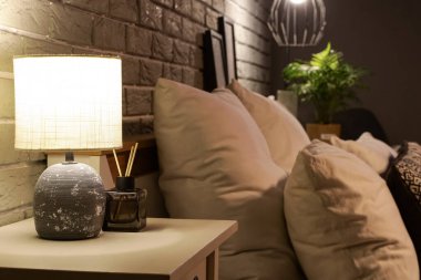 Karanlık yatak odasındaki masada sazlık yayıcı ile parlayan lamba.