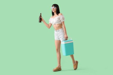 Portatif buzdolabı ve yeşil arka planda soğuk bira şişesi olan genç bir kadın.