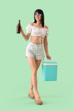 Portatif buzdolabı ve yeşil arka planda soğuk bira şişesi olan genç bir kadın.