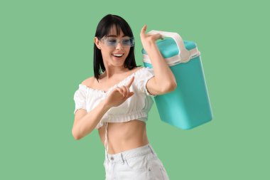 Yeşil arka planda taşınabilir buzdolabı olan genç bir kadın.