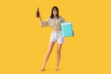 Portatif buzdolabı ve sarı arka planda soğuk bira şişesi olan genç bir kadın.