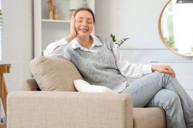 Oturma odasındaki gri koltukta oturan gülümseyen genç kadın.