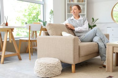 Oturma odasındaki gri koltukta oturan gülümseyen genç kadın.