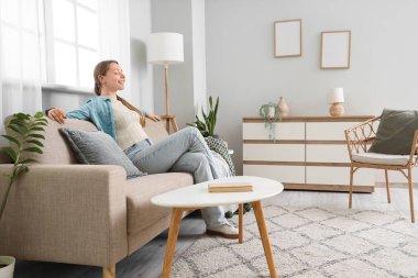 Oturma odasındaki gri koltukta oturan gülümseyen genç kadın.