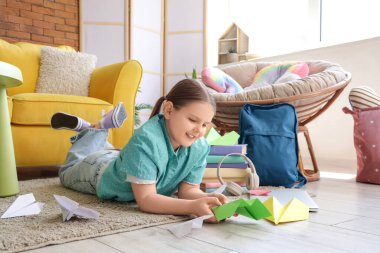 Evdeki halıda kağıt uçakları olan tatlı bir kız.