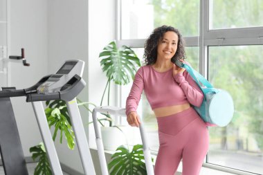 Spor çantalı olgun bir kadın spor salonunda koşu bandının yanında.