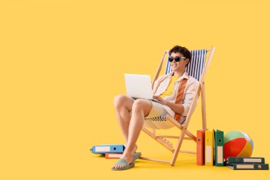 Genç iş adamı sarı arka planda dizüstü bilgisayar kullanıyor. Yaz tatili