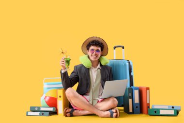Dizüstü bilgisayarı ve kokteyli olan genç işadamı sarı arka planda yaz tatilini bekliyor.