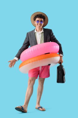 Yüzme yüzükleri ve evrak çantalı genç işadamı mavi arka planda yaz tatilini bekliyor.