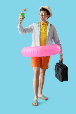 Kokteyl ve evrak çantalı genç işadamı mavi arka planda yaz tatilini bekliyor.