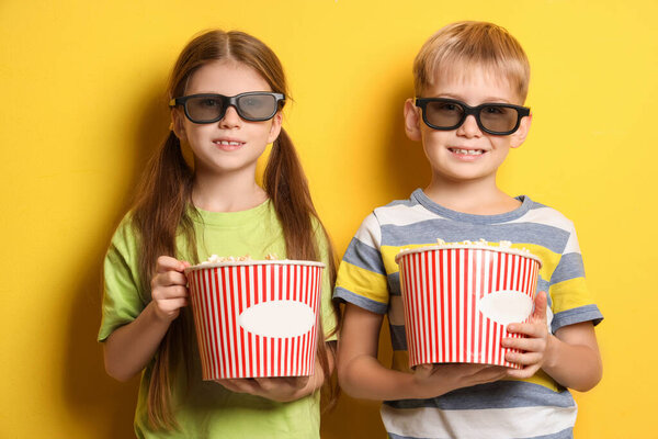 Little children in 3D glasses with popcorn on yellow background