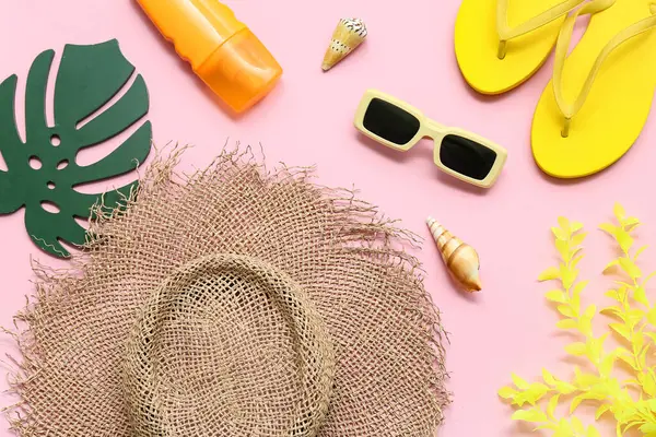 Terlik, güneş kremi, deniz kabuğu ve pembe arka planda şapkası olan hasır çanta. Yaz konsepti
