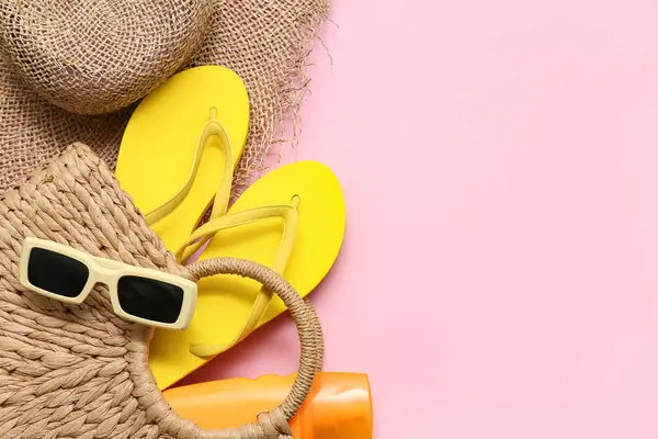 Parmak arası terlik, güneş kremi ve pembe arka planda şapka olan hasır çanta. Yaz konsepti