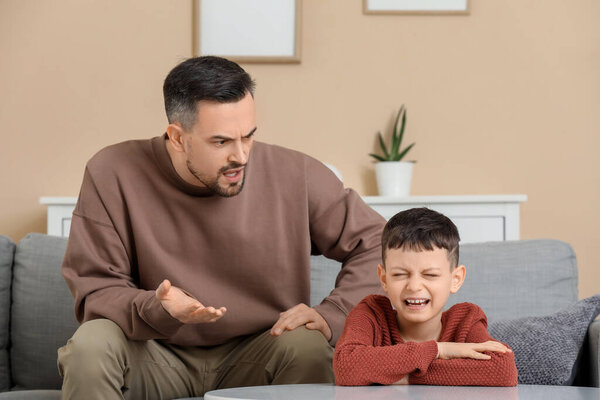 Отец ссорится со своим плачущим сыном дома