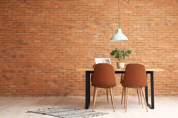 Laptoplu yemek masası ve odada tuğla duvarın yanına bitki.