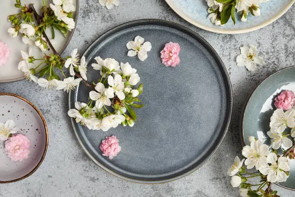 Çiçek açan dalları ve gri arka planda güzel çiçekleri olan farklı temiz tabaklar.