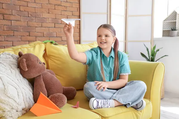Evdeki kanepede kağıt uçakla oturan tatlı kız.