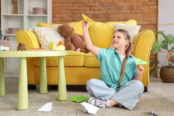 Evdeki halıda kağıt uçakları olan tatlı bir kız.