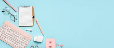 Mavi zemin üzerinde defter, gözlük ve klavye olan kompozisyon. Üst görünüm