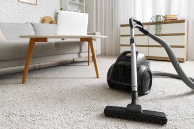 Elektrikli süpürge, kanepe ve klozetle aydınlık oturma odasının içinde.