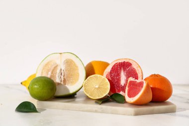 Tepsi ve lezzetli narenciye meyveleri beyaz duvarın yanındaki mermer masada.