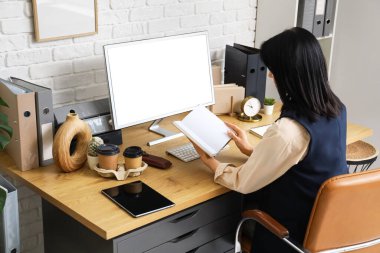 Kitap okuyan ve bilgisayarın başında oturan genç bir kadın.