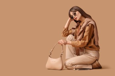 Kravat, el çantası ve güneş gözlüklü şık gömlekli güzel bir bayan bej arka planda oturuyor.