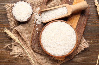 Tahta zemin üzerinde buğday olan kase ve kepçe çiğ pirinç.