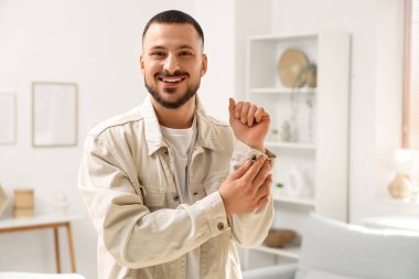 Genç adam evde kot ceket düğmelerini ilikliyor.