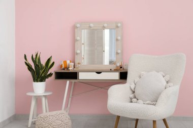 Ayna, koltuk, makyaj malzemesi ve makyaj masası olan şık bir makyaj odası.