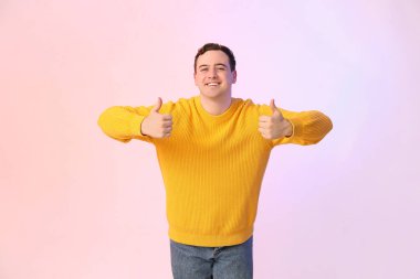 Yakışıklı, genç ve mutlu bir adam. Renkli arka planda baş parmak hareketlerini gösteriyor.
