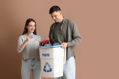 Çöpleri kahverengi arka planda çöp kutusuna koyan genç bir çift. Küresel Geri Dönüşüm Günü