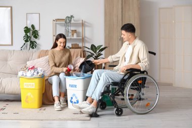 Tekerlekli sandalyedeki genç adam ve kız arkadaşı evdeki çöp kutularını düzenliyor. Küresel Geri Dönüşüm Günü