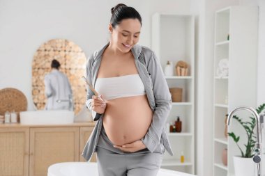 Banyoda diş fırçasıyla hamile bir kadın.