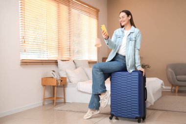 Otel odasında çantanın üzerinde cep telefonu kullanan bir kadın turist.