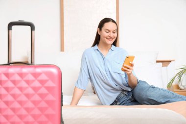 Otel odasında cep telefonu kullanan genç bir kadın.