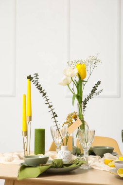 Odada ışık duvarının yanında bahar çiçekleri olan masa ayarı