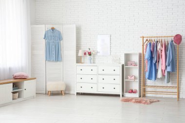 Açık renk soyunma odasının içinde askılık, çekmeceler ve katlanır ekran var.