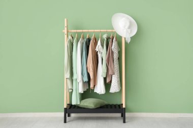 Elbise askısı, şık kıyafetler ve yeşil duvarın yanında şapka.