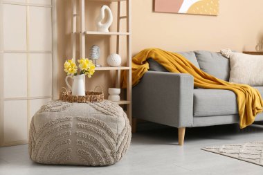 Oturma odasının içinde kanepe, raf ünitesi ve vazoda güzel nergisler var.