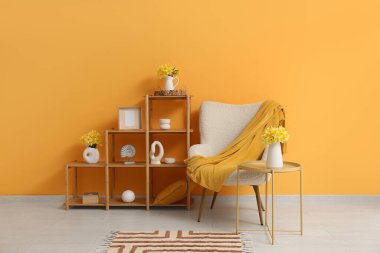 Koltuk, raf ünitesi ve masadaki vazolarda güzel nergis buketleri olan bir oda.