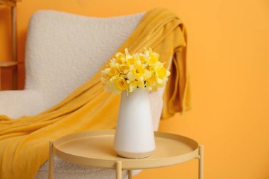 güzel nergis vazosu sehpanın üzerinde sarı duvara yaslanmış bir sehpa.