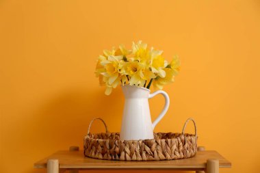 Sarı duvarın yanındaki raf ünitesinde vazo vazo dolusu nergis buketi.